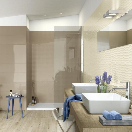 Bagno moderno con parete rivestita in piastrelle beige lucide e lavabo bianco su superficie in legno chiaro.
